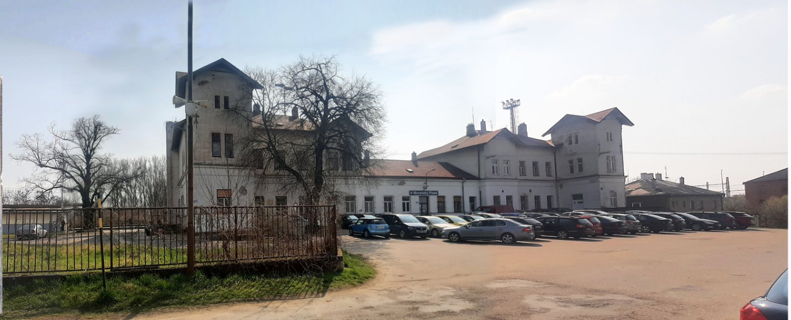 Nádraží dnes - opuštěná budova s oprýskanou fasádou a parkovištěm bez ladu